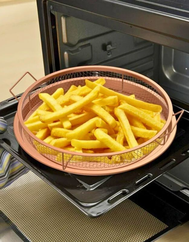 French fries cooking in a round mesh air fryer basket inside an oven.
